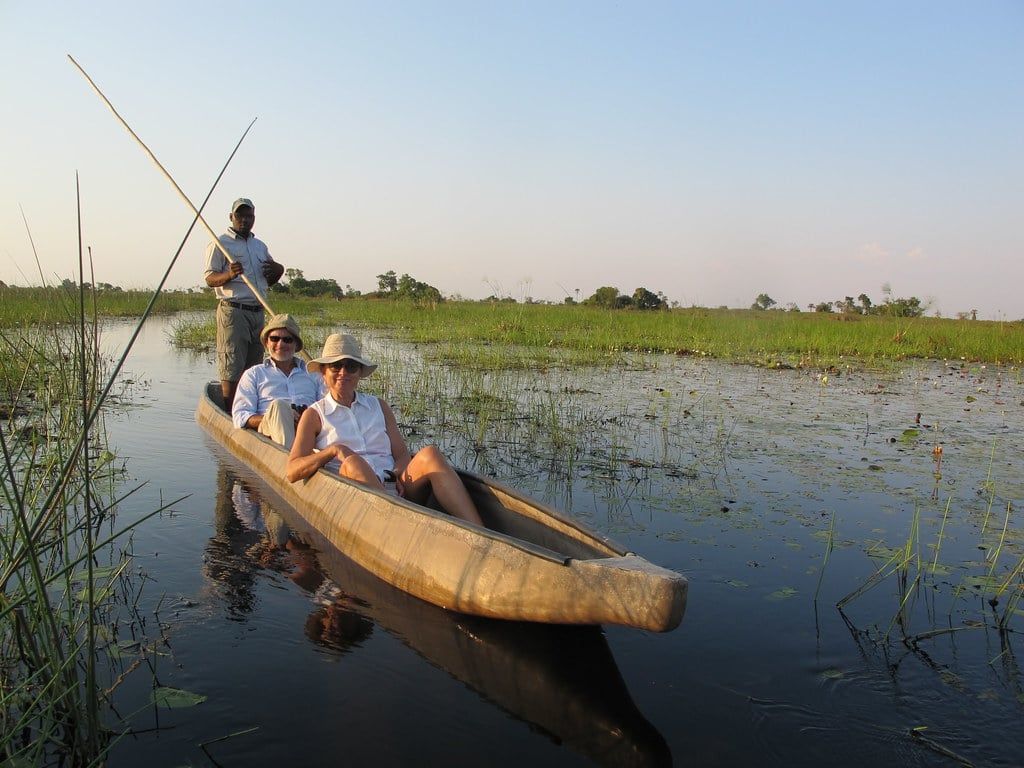 Tourists ride in a traditional mokoro canoe guided by a poler through a flooded channel in the Okavango Delta.