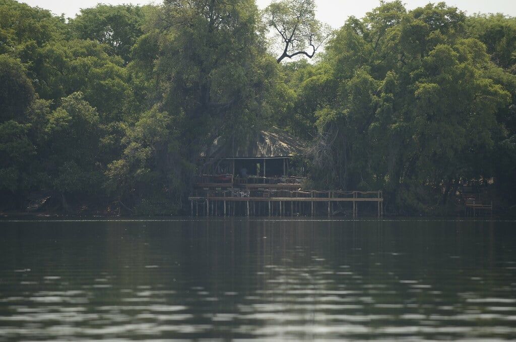 Eine Safari-Lodge mit erhöhter Holzterrasse, eingebettet in üppige Bäume am Wasser im Okavango-Delta.
